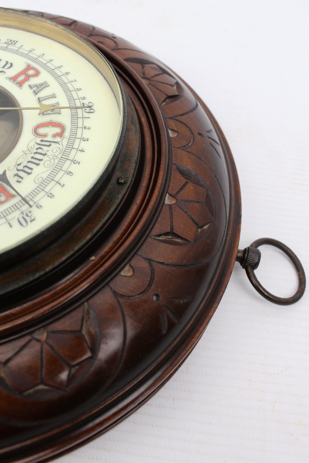 A circular Victorian walnut wall barometer featuring a carved wooden border, a brass hanging ring, and an exposed brass skeleton movement within an enamel dial. View XI