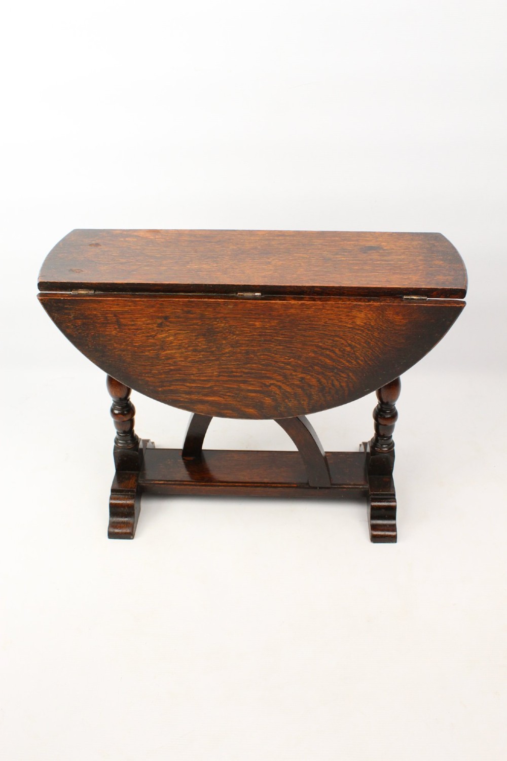 A dark oak drop-leaf coffee table featuring hinged side flaps, turned legs, and a sturdy trestle base. View II