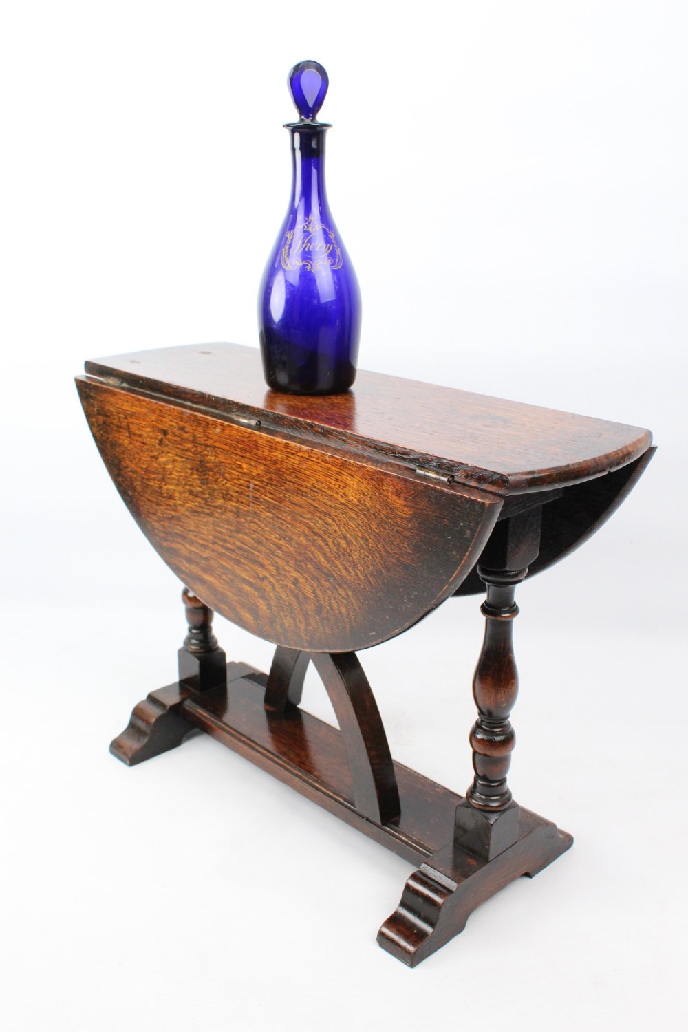 A dark oak drop-leaf coffee table featuring hinged side flaps, turned legs, and a sturdy trestle base. View III