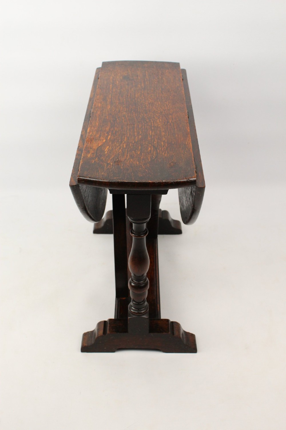 A dark oak drop-leaf coffee table featuring hinged side flaps, turned legs, and a sturdy trestle base. View IV