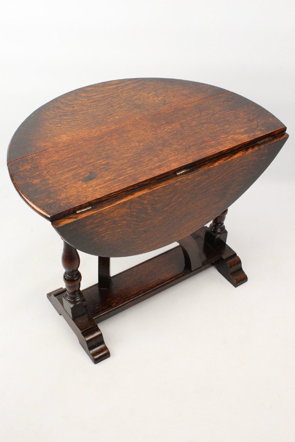 A dark oak drop-leaf coffee table featuring hinged side flaps, turned legs, and a sturdy trestle base. View VII