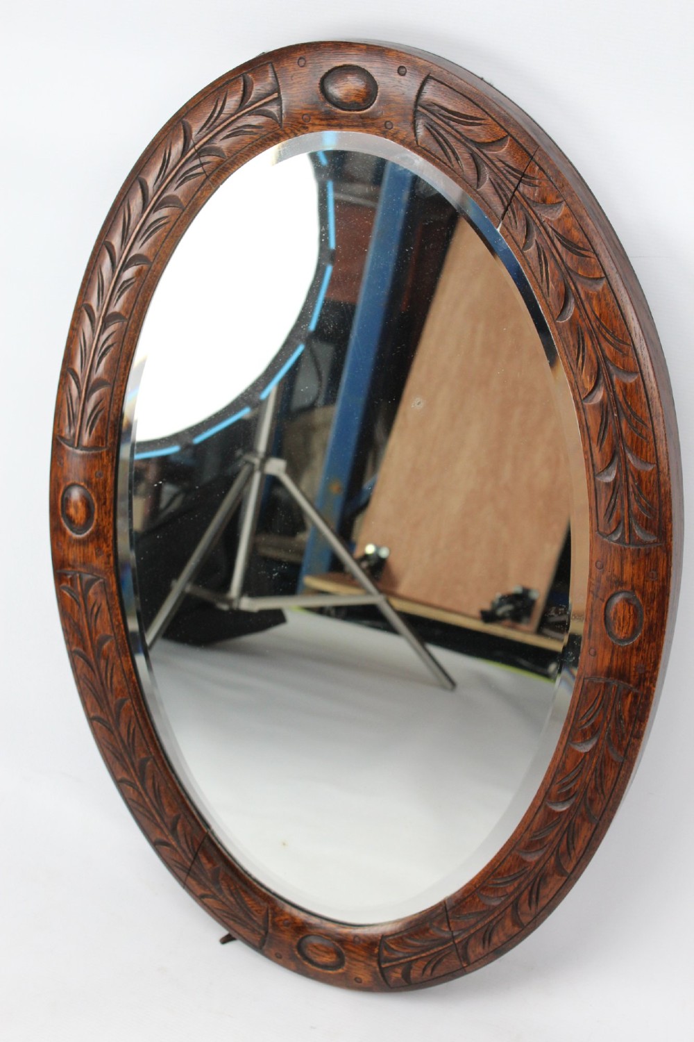 An Edwardian oval wall mirror featuring a carved dark oak frame decorated with leaf motifs and rounded bosses. View II