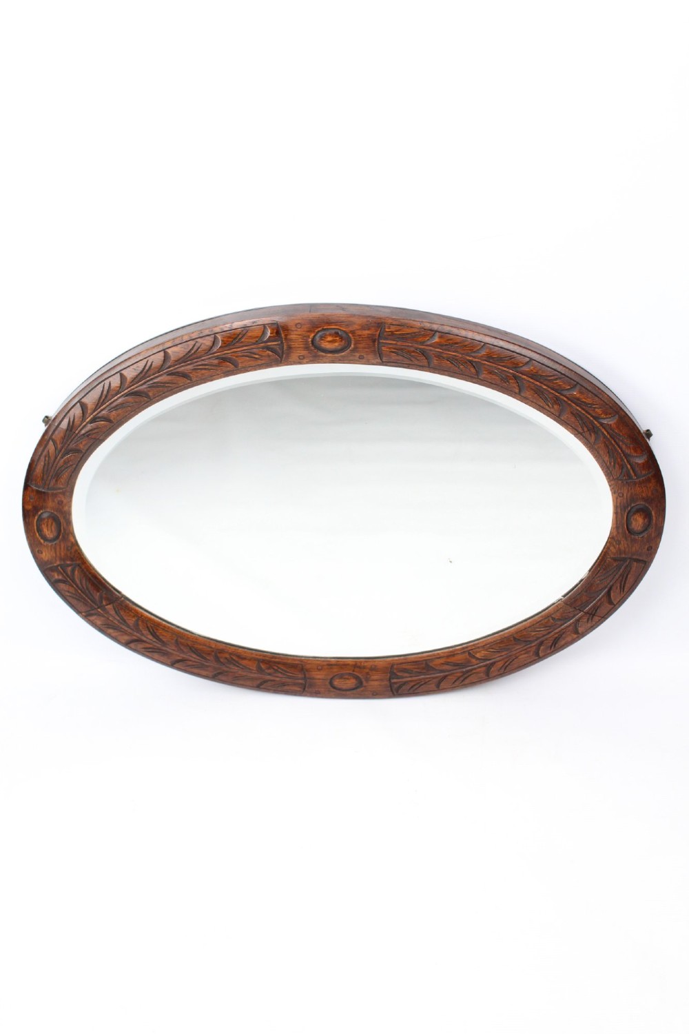 An Edwardian oval wall mirror featuring a carved dark oak frame decorated with leaf motifs and rounded bosses. View III