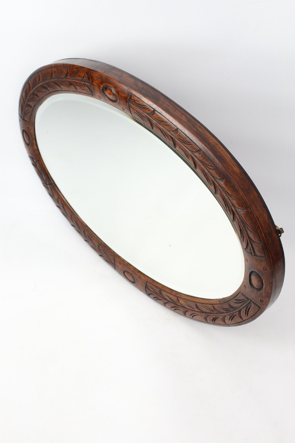 An Edwardian oval wall mirror featuring a carved dark oak frame decorated with leaf motifs and rounded bosses. View IV