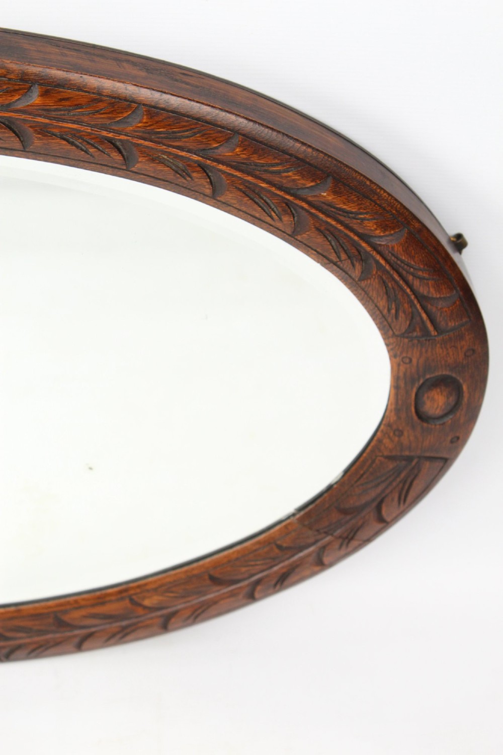 An Edwardian oval wall mirror featuring a carved dark oak frame decorated with leaf motifs and rounded bosses. View VI