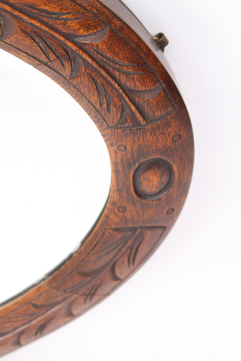 An Edwardian oval wall mirror featuring a carved dark oak frame decorated with leaf motifs and rounded bosses. View VII