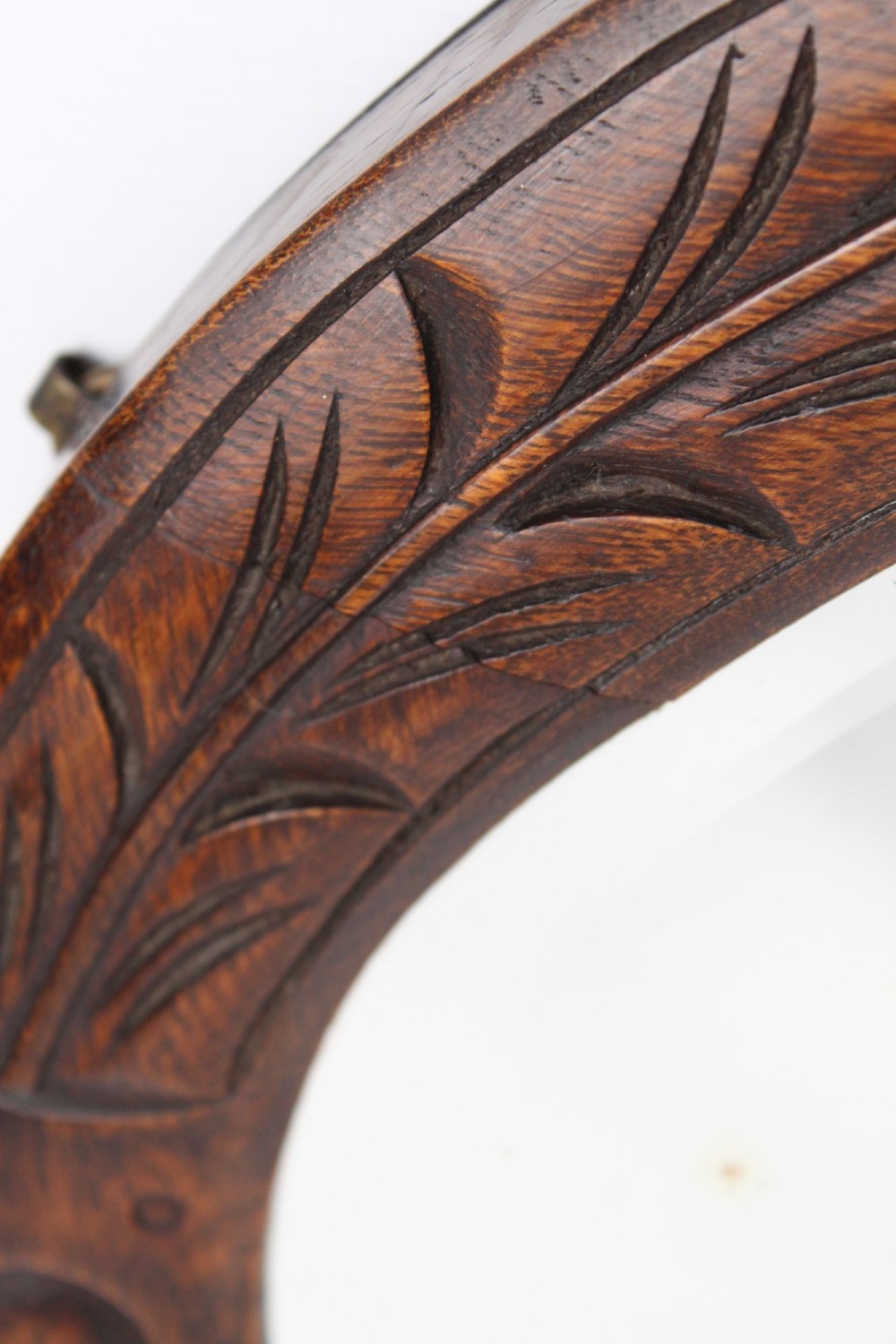 An Edwardian oval wall mirror featuring a carved dark oak frame decorated with leaf motifs and rounded bosses. View VIII