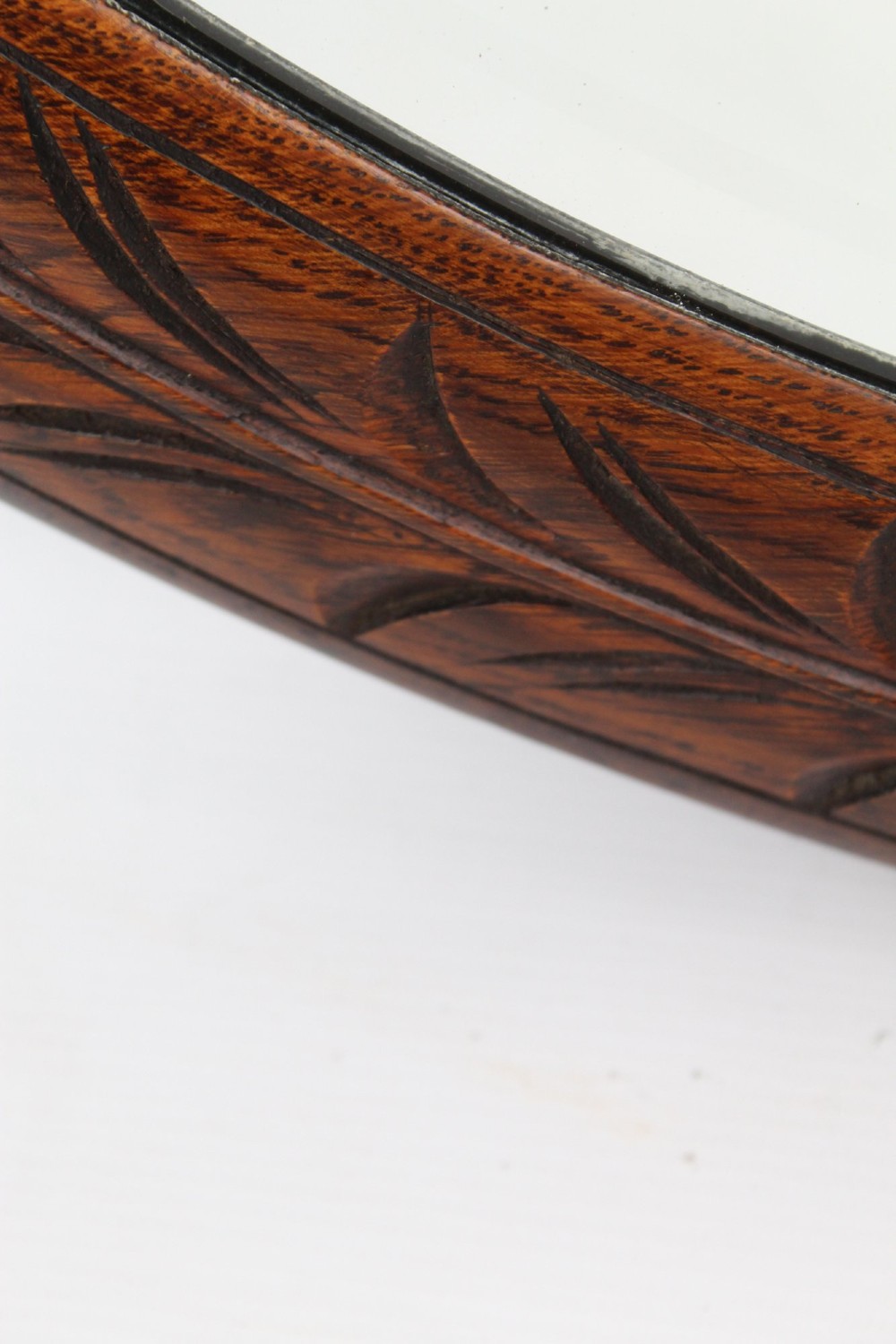 An Edwardian oval wall mirror featuring a carved dark oak frame decorated with leaf motifs and rounded bosses. View IX