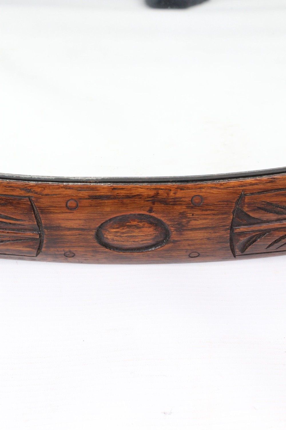 An Edwardian oval wall mirror featuring a carved dark oak frame decorated with leaf motifs and rounded bosses. View X