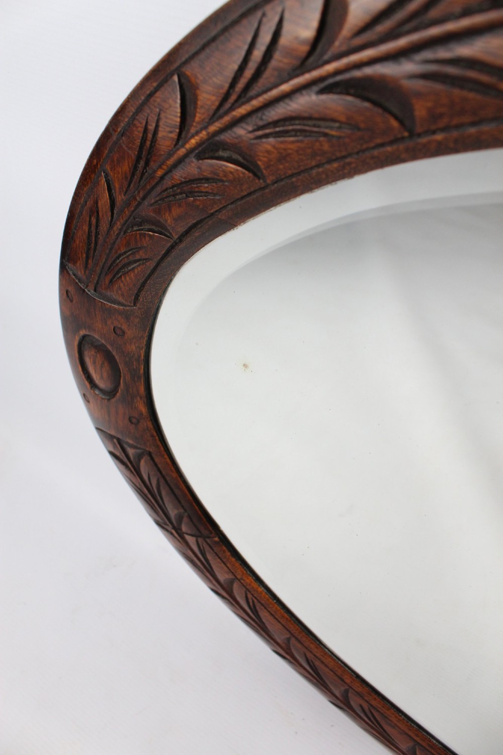 An Edwardian oval wall mirror featuring a carved dark oak frame decorated with leaf motifs and rounded bosses. View XI