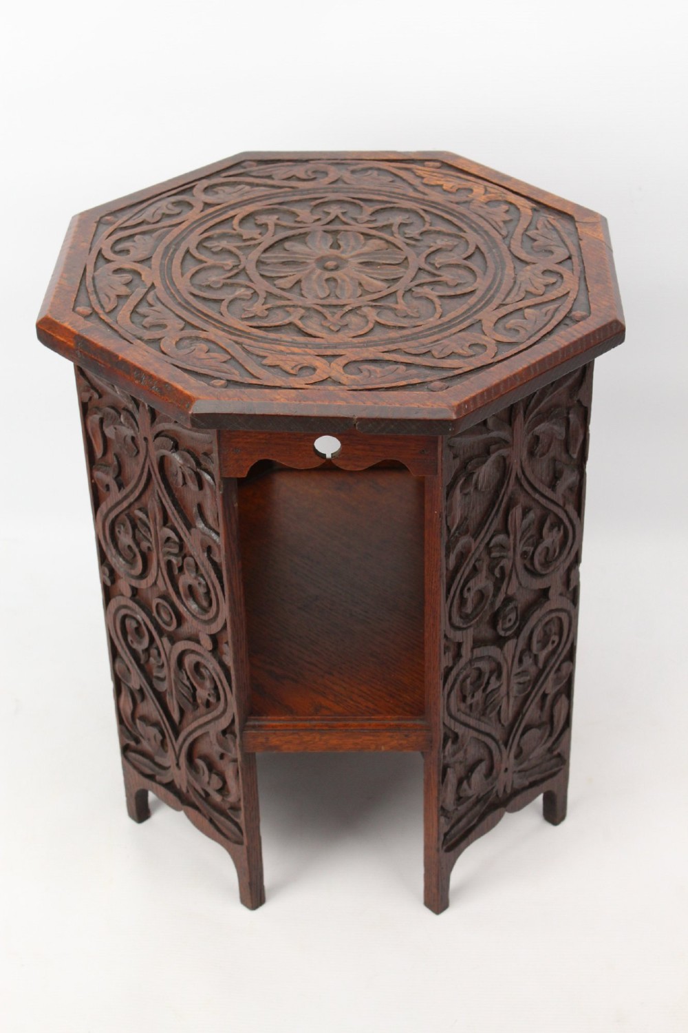 An Edwardian hexagonal dark oak side table featuring intricate relief carving on the top surface and side panels.