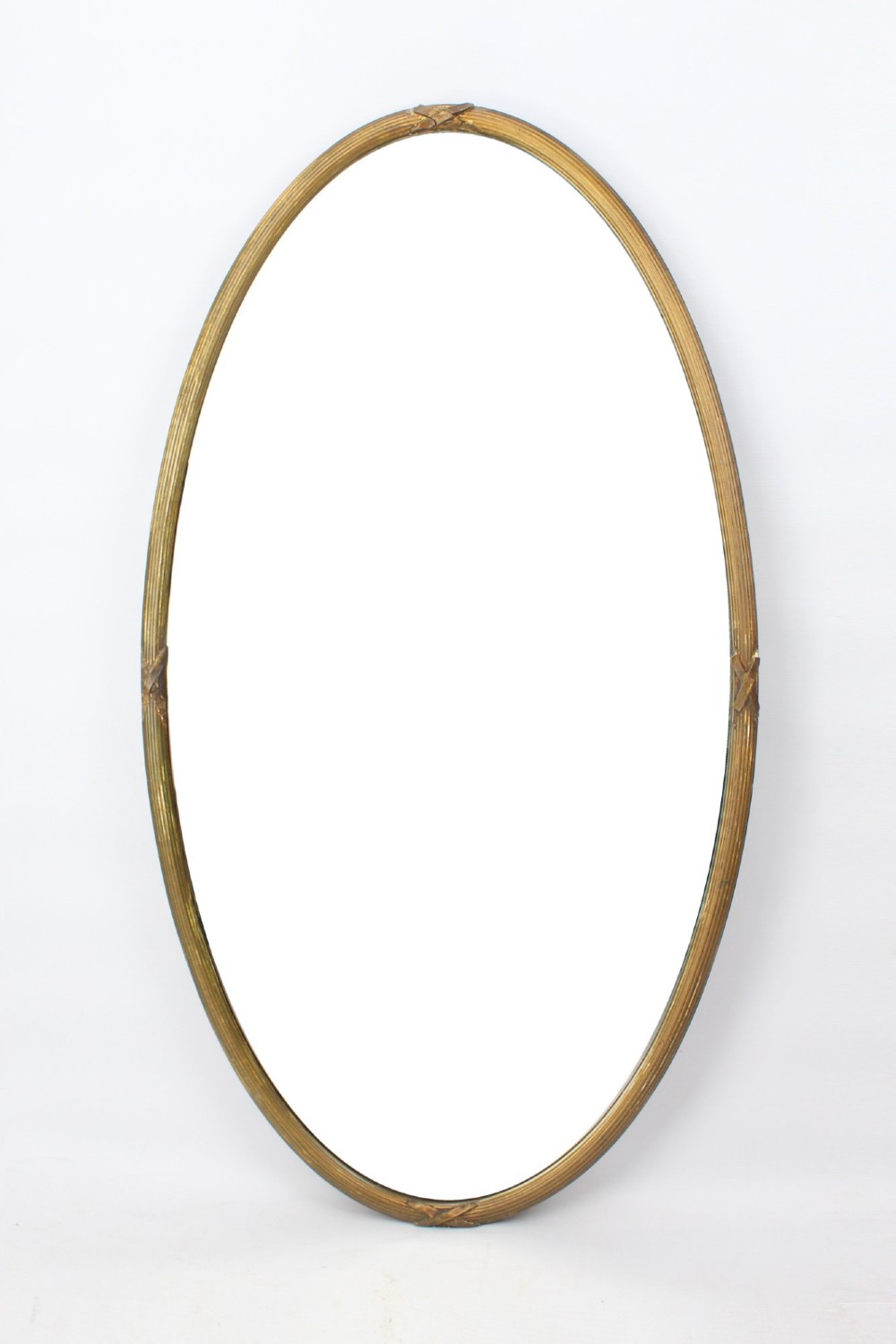 A large Victorian oval wall mirror featuring a gilded reeded frame with decorative cross-ribbon accents at four points.