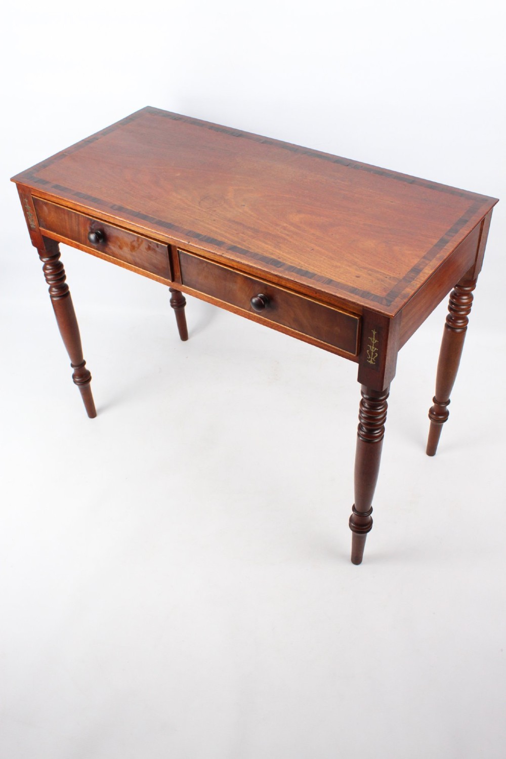 A Regency mahogany writing desk featuring brass inlaid corner stiles, two frieze drawers with wooden knobs, and turned legs. View II