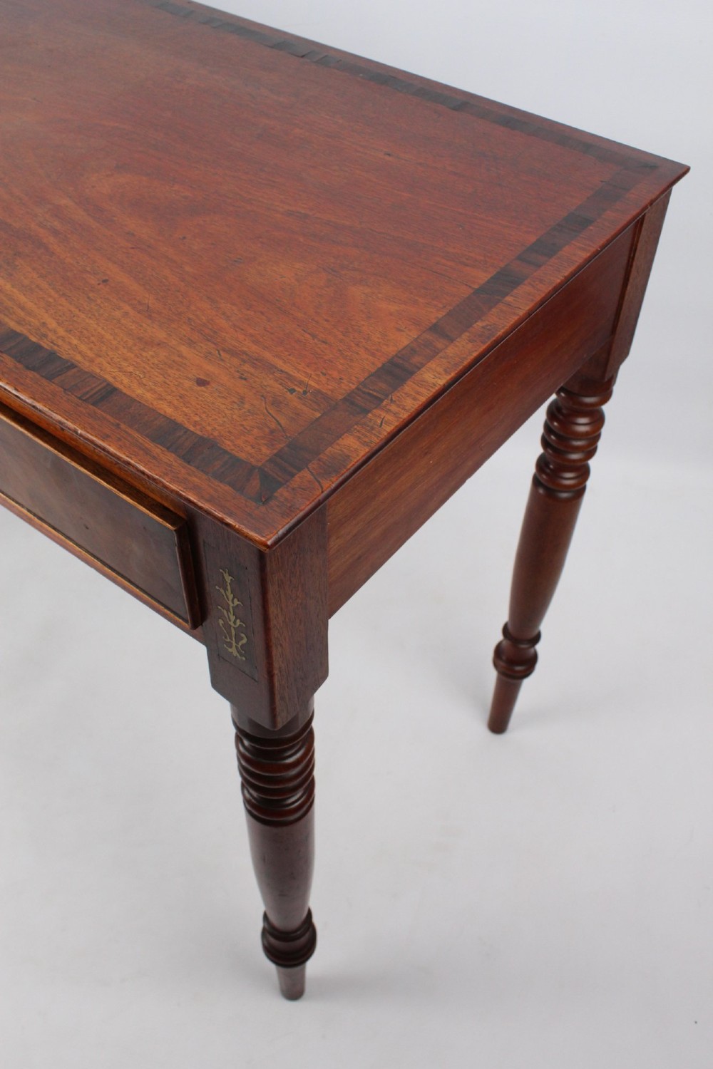 A Regency mahogany writing desk featuring brass inlaid corner stiles, two frieze drawers with wooden knobs, and turned legs. View V