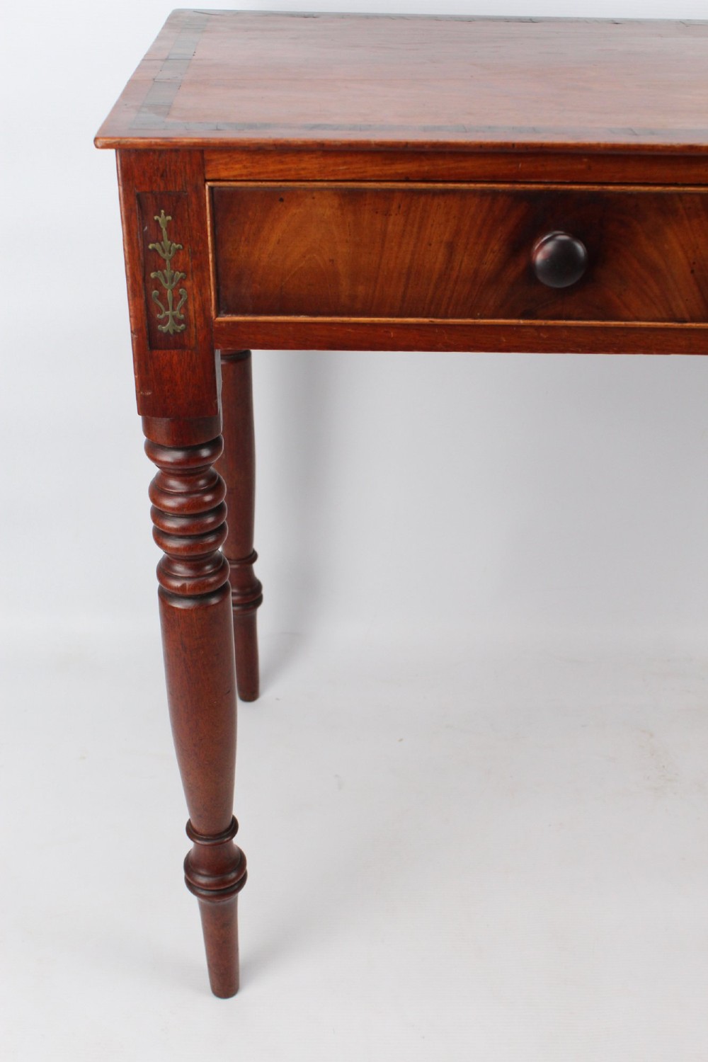 A Regency mahogany writing desk featuring brass inlaid corner stiles, two frieze drawers with wooden knobs, and turned legs. View VI