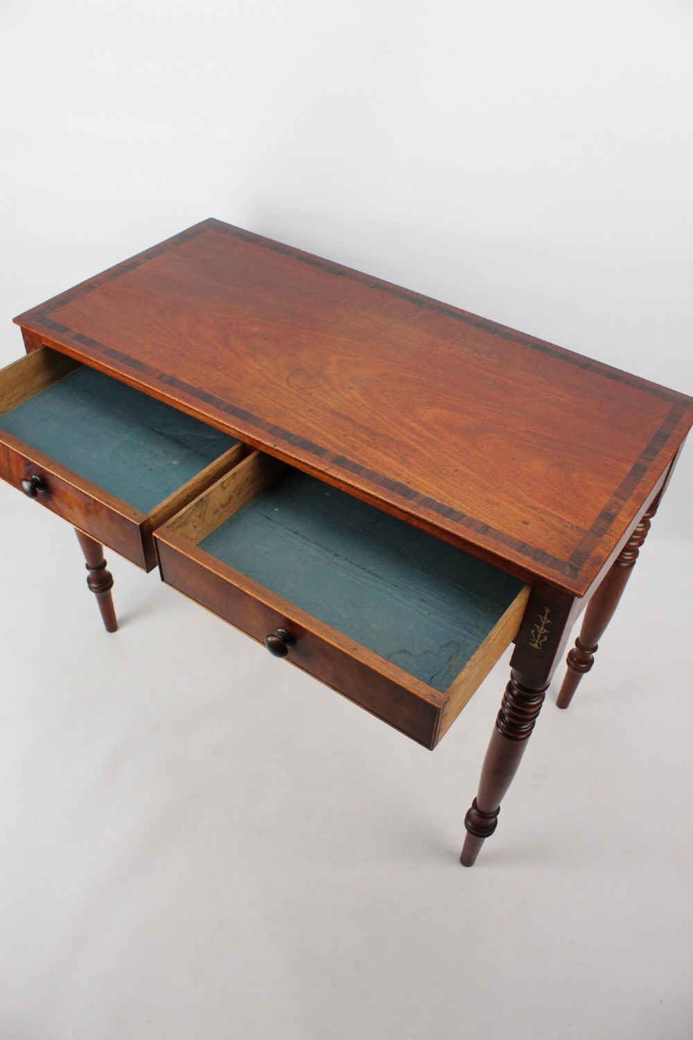 A Regency mahogany writing desk featuring brass inlaid corner stiles, two frieze drawers with wooden knobs, and turned legs. View X