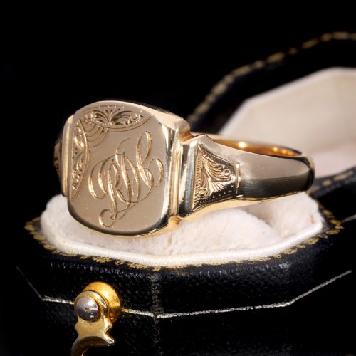 fig 1. A yellow gold signet ring featuring a cushion-shaped face hand-engraved with cursive initials and delicate scrollwork details on the shoulders.