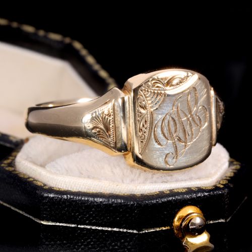 fig 2. A yellow gold signet ring featuring a cushion-shaped face hand-engraved with cursive initials and delicate scrollwork details on the shoulders.