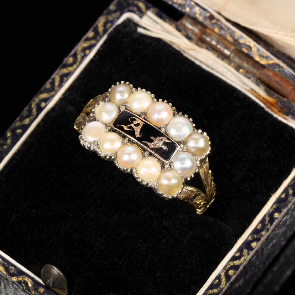 A Victorian gold ring featuring a central rectangular black enamel plaque with gold gothic initials surrounded by twelve seed pearls and chased shoulders.