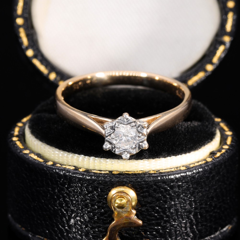 A yellow gold solitaire ring featuring a round clear diamond held within a star-shaped white metal illusion setting.