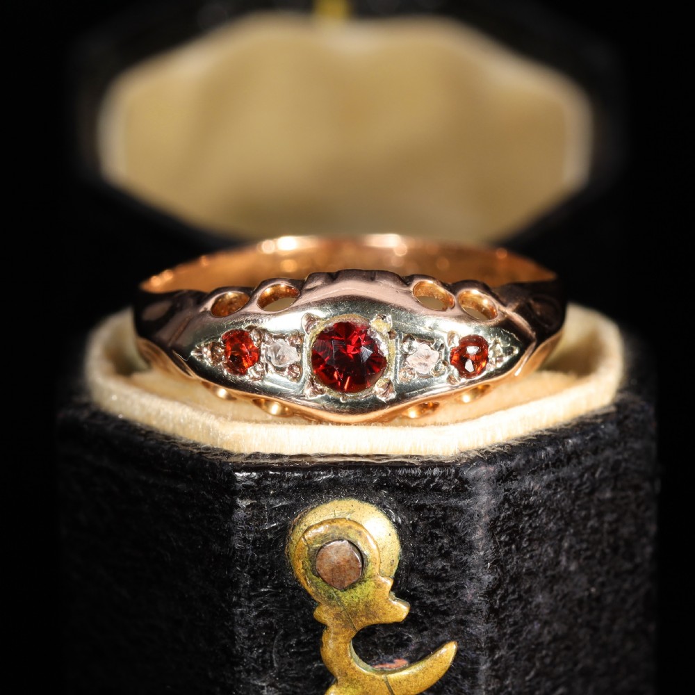 A vintage 1929 gold ring featuring a carved bridge setting mounted with central deep red garnets and small accent diamonds.