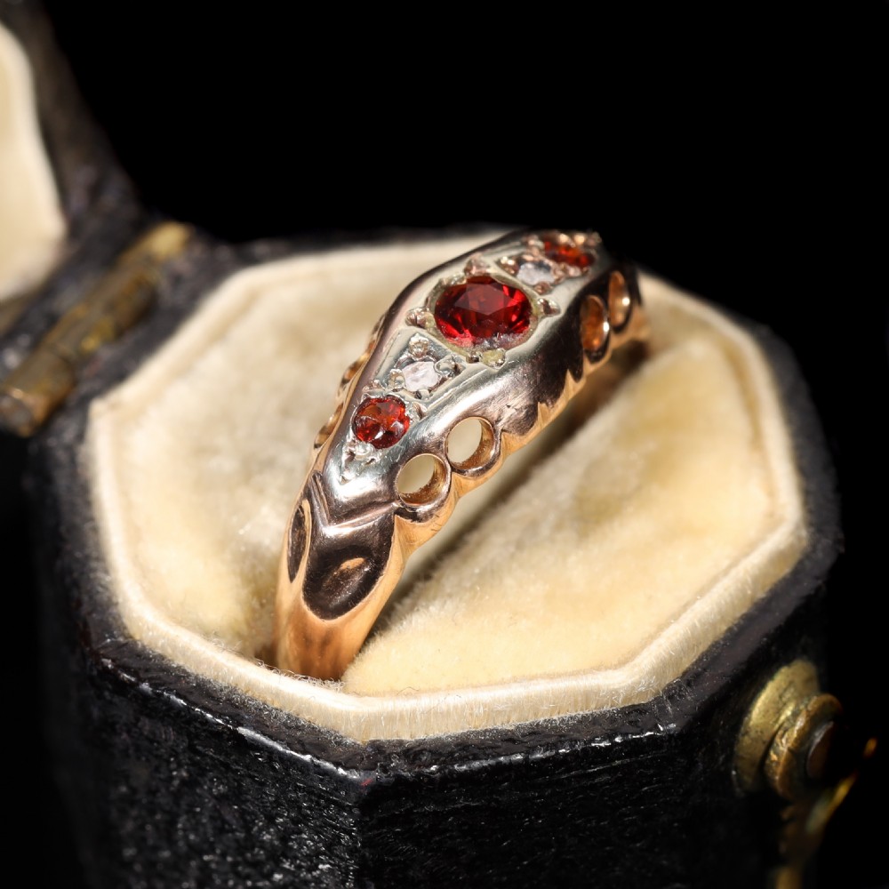 A vintage 1929 gold ring featuring a carved bridge setting mounted with central deep red garnets and small accent diamonds. View II