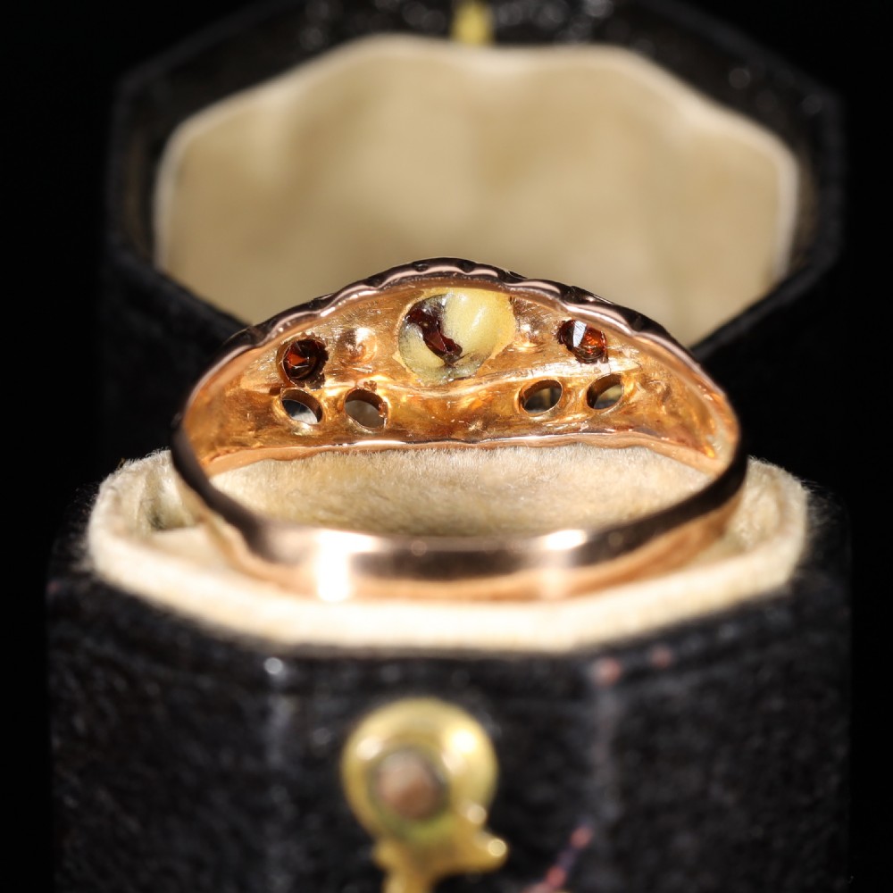 A vintage 1929 gold ring featuring a carved bridge setting mounted with central deep red garnets and small accent diamonds. View VII