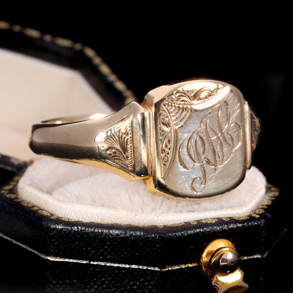 A yellow gold signet ring featuring a cushion-shaped face hand-engraved with cursive initials and delicate scrollwork details on the shoulders. View III