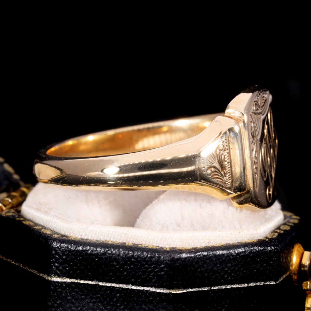 A yellow gold signet ring featuring a cushion-shaped face hand-engraved with cursive initials and delicate scrollwork details on the shoulders. View IV