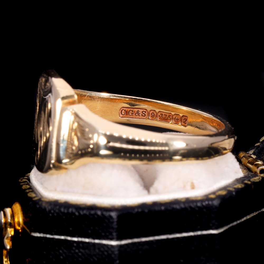A yellow gold signet ring featuring a cushion-shaped face hand-engraved with cursive initials and delicate scrollwork details on the shoulders. View V