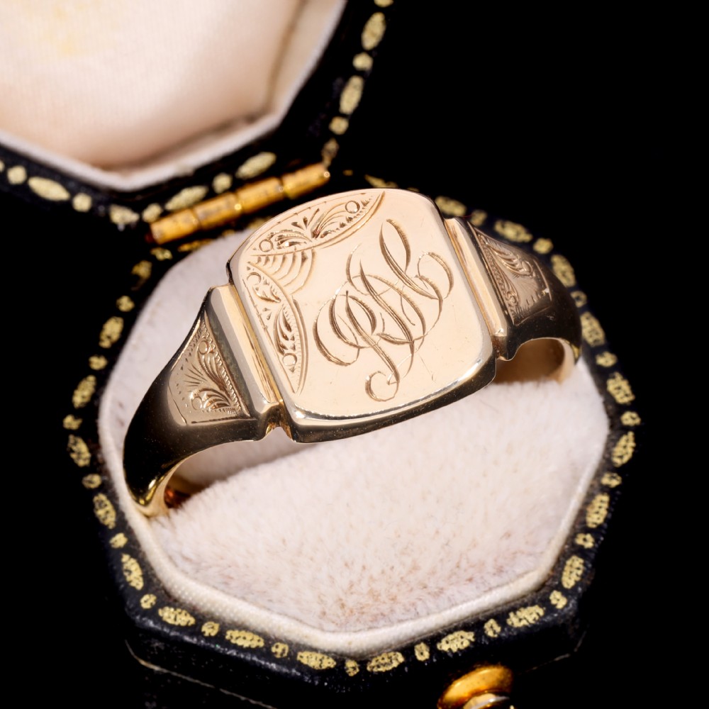 A yellow gold signet ring featuring a cushion-shaped face hand-engraved with cursive initials and delicate scrollwork details on the shoulders. View VIII