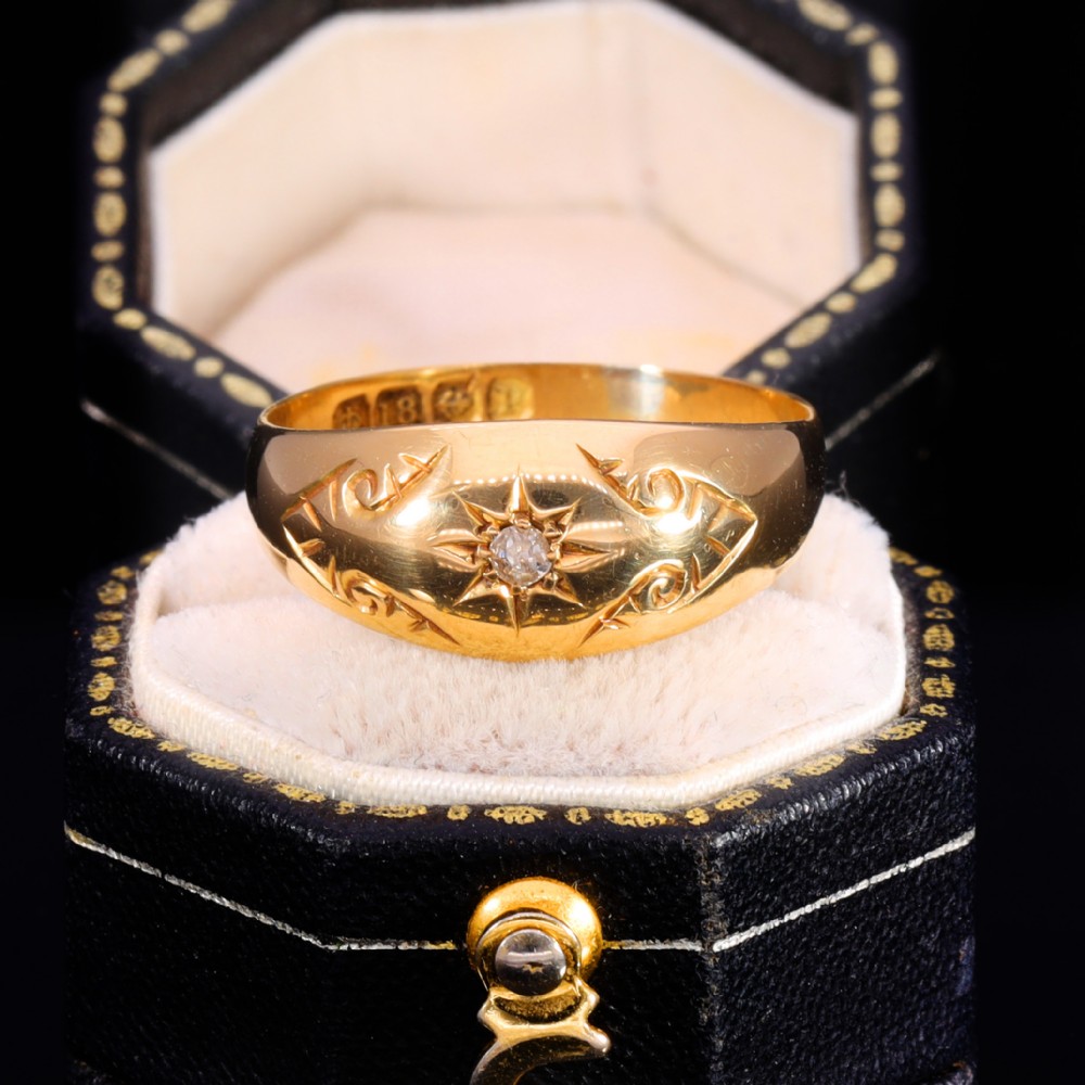 An 18ct yellow gold Victorian band ring featuring a starburst-set diamond surrounded by hand-carved scroll engraving and visible internal hallmarks.
