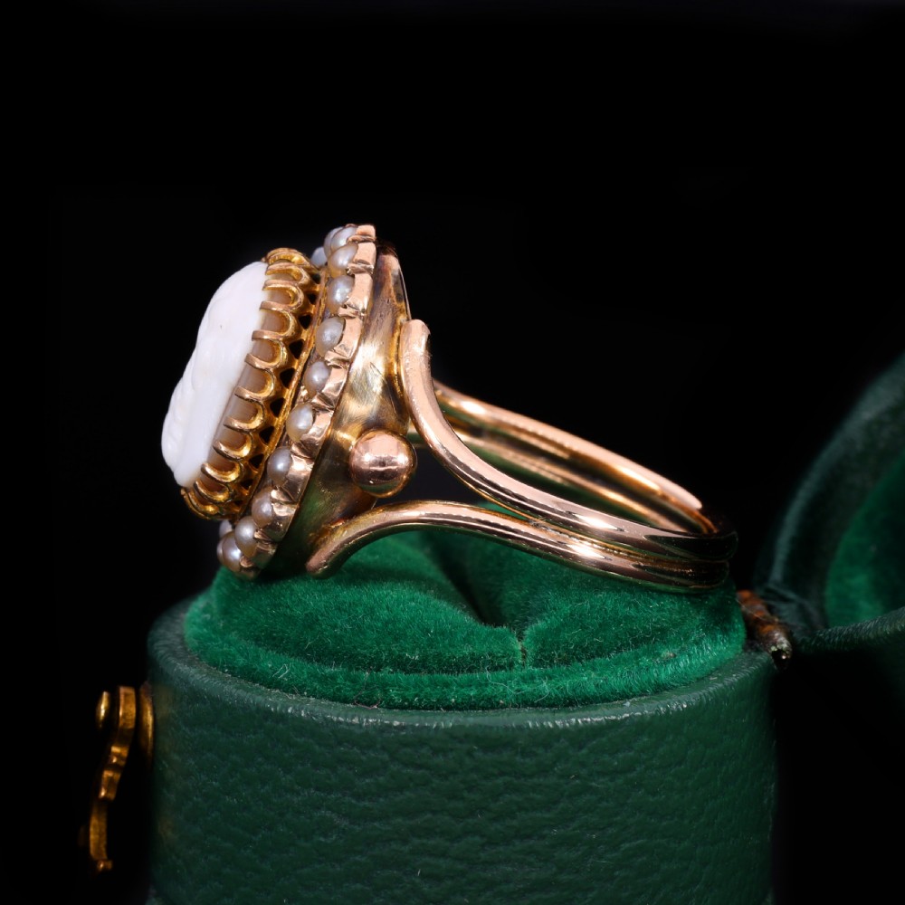 A Victorian yellow gold ring set with an oval carved shell cameo profile encircled by a halo of seed pearls. View V