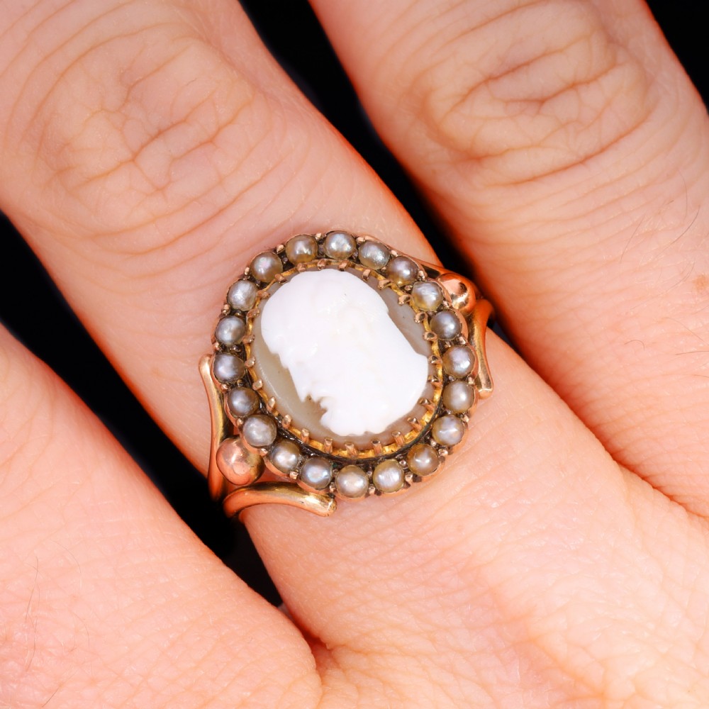 A Victorian yellow gold ring set with an oval carved shell cameo profile encircled by a halo of seed pearls. View VII
