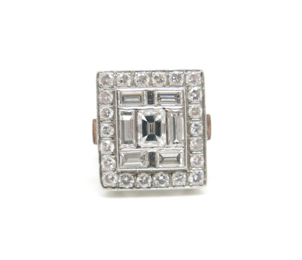 A square Art Deco platinum plaque ring set with geometric baguette and round brilliant diamonds with millgrain borders.