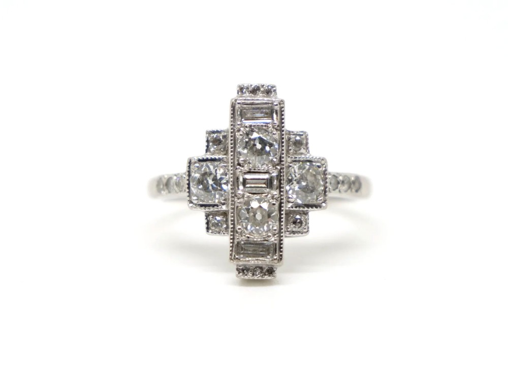 An Art Deco 18ct gold ring featuring a geometric stepped plaque design set with round old cut diamonds and baguette cut diamonds.