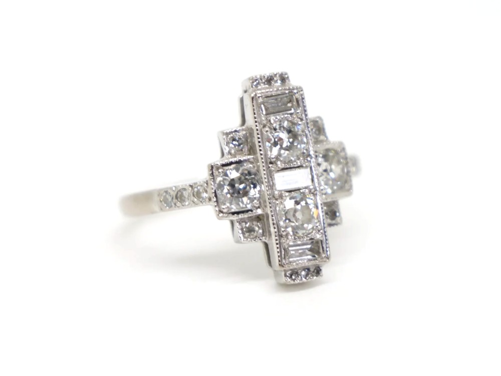 An Art Deco 18ct gold ring featuring a geometric stepped plaque design set with round old cut diamonds and baguette cut diamonds. View II