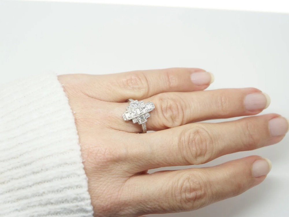 An Art Deco 18ct gold ring featuring a geometric stepped plaque design set with round old cut diamonds and baguette cut diamonds. View V