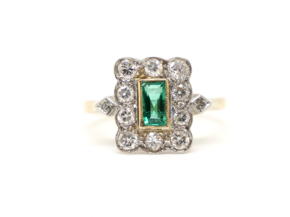 An Art Deco style ring featuring a central emerald-cut green emerald surrounded by a scalloped border of round diamonds set in white metal on a yellow gold band.