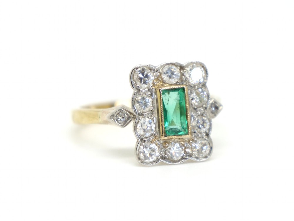 An Art Deco style ring featuring a central emerald-cut green emerald surrounded by a scalloped border of round diamonds set in white metal on a yellow gold band. View II