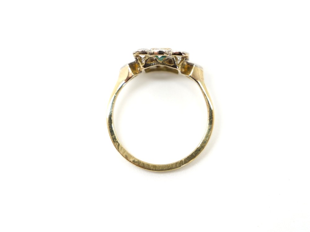 An Art Deco style ring featuring a central emerald-cut green emerald surrounded by a scalloped border of round diamonds set in white metal on a yellow gold band. View IV