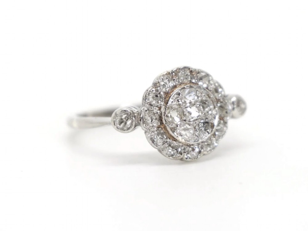 An Art Deco platinum cluster ring set with old cut diamonds arranged in a circular floral pattern with accent diamonds on the shoulders. View II