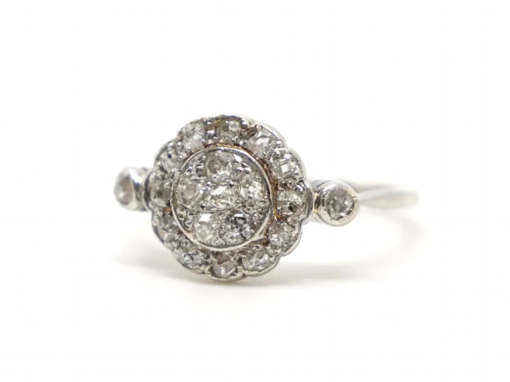 An Art Deco platinum cluster ring set with old cut diamonds arranged in a circular floral pattern with accent diamonds on the shoulders. View III