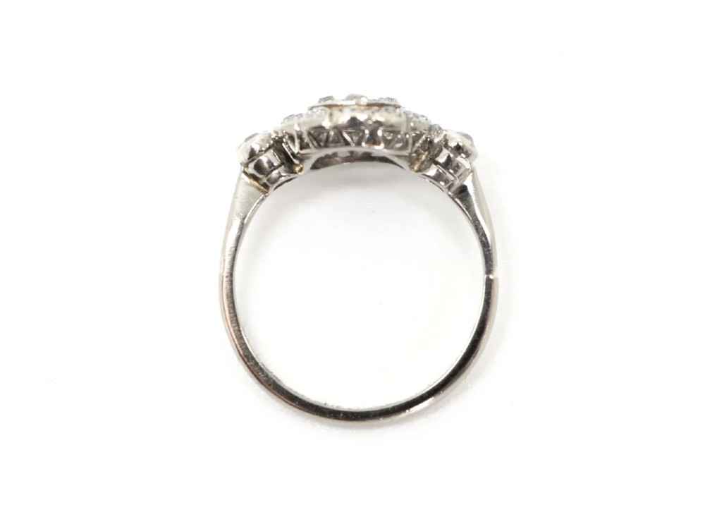 An Art Deco platinum cluster ring set with old cut diamonds arranged in a circular floral pattern with accent diamonds on the shoulders. View IV