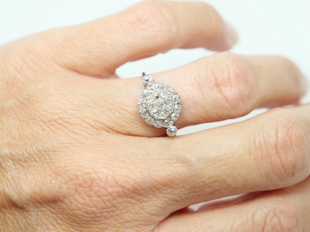 An Art Deco platinum cluster ring set with old cut diamonds arranged in a circular floral pattern with accent diamonds on the shoulders. View V