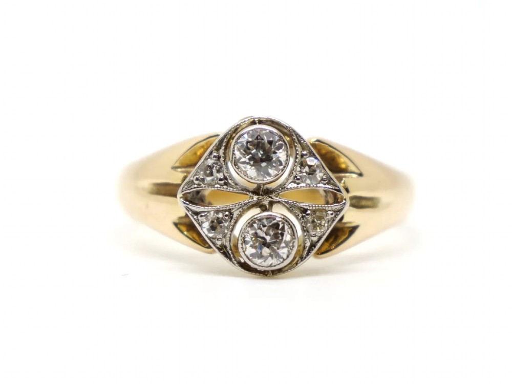 An Art Deco two-stone diamond ring crafted in 18ct yellow gold with a geometric white metal setting featuring two main diamonds and small accent stones.