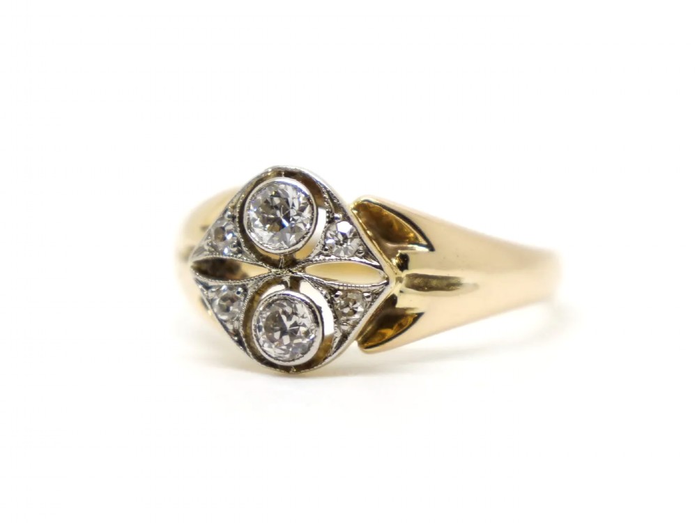 An Art Deco two-stone diamond ring crafted in 18ct yellow gold with a geometric white metal setting featuring two main diamonds and small accent stones. View II