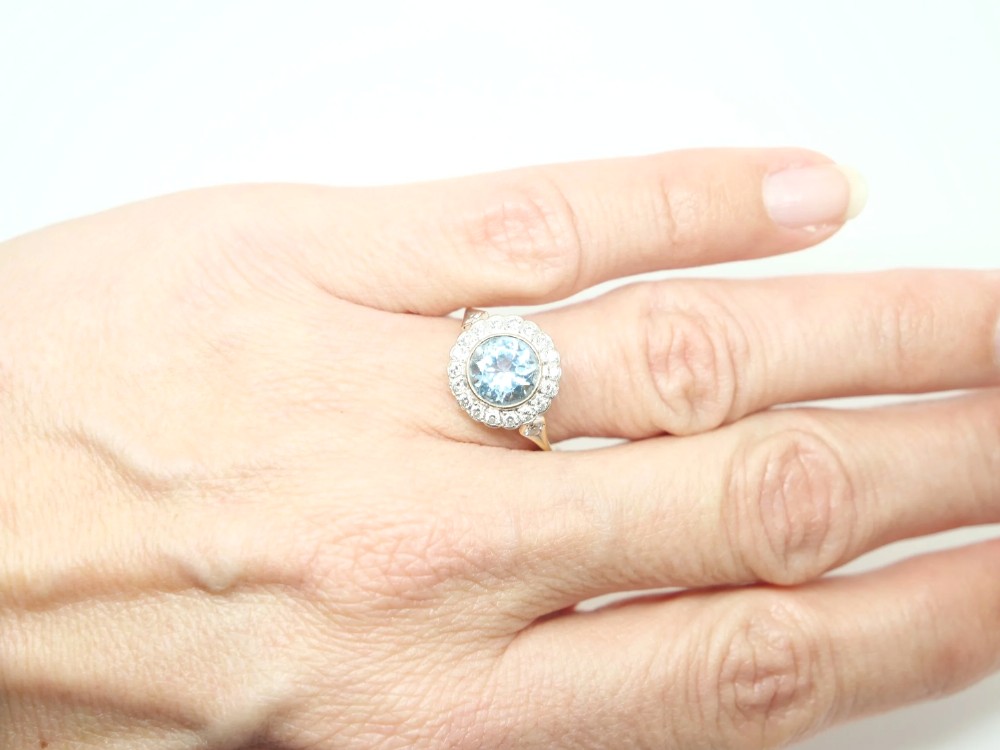 A round-cut light blue aquamarine ring surrounded by a circular diamond halo setting on a gold band. View VI