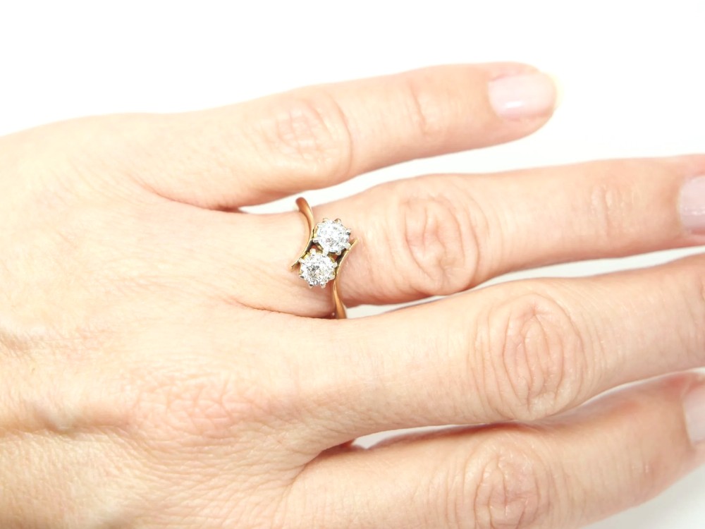 An 18ct yellow gold ring featuring a crossover band set with two round brilliant diamonds in multi-claw settings. View V