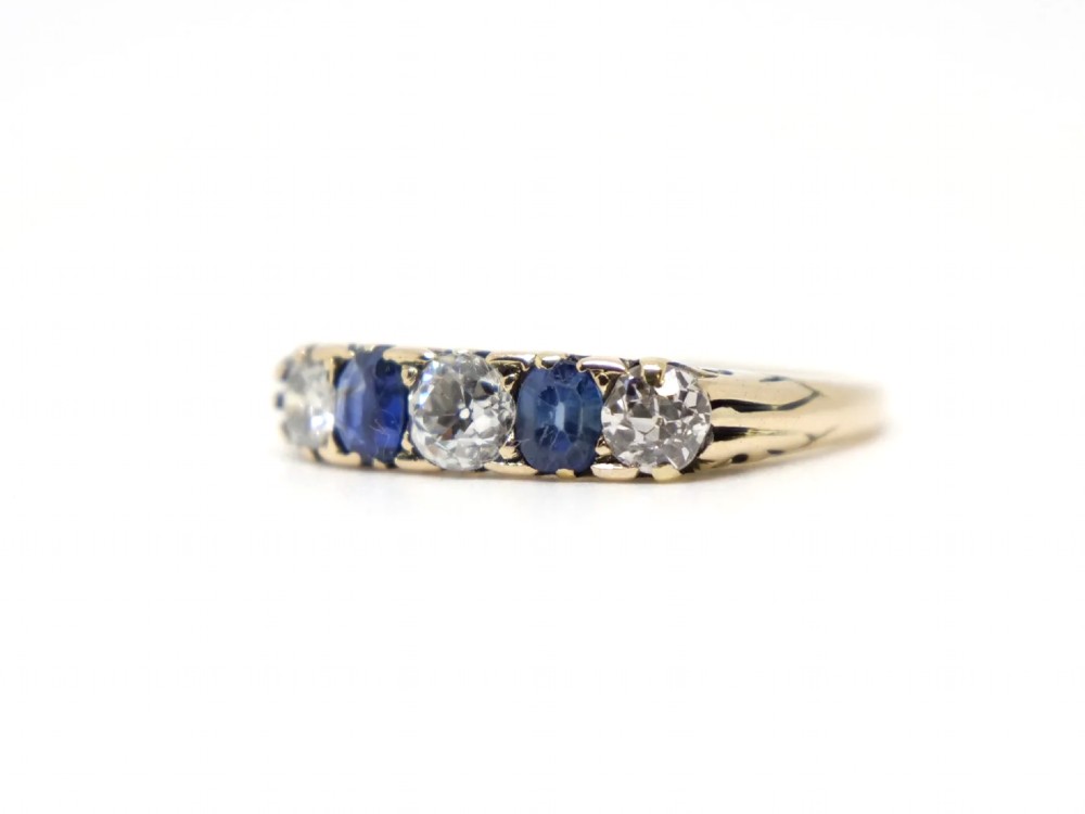 An 18ct yellow gold five-stone ring set with alternating round diamonds and oval blue sapphires in claw mounts. View III